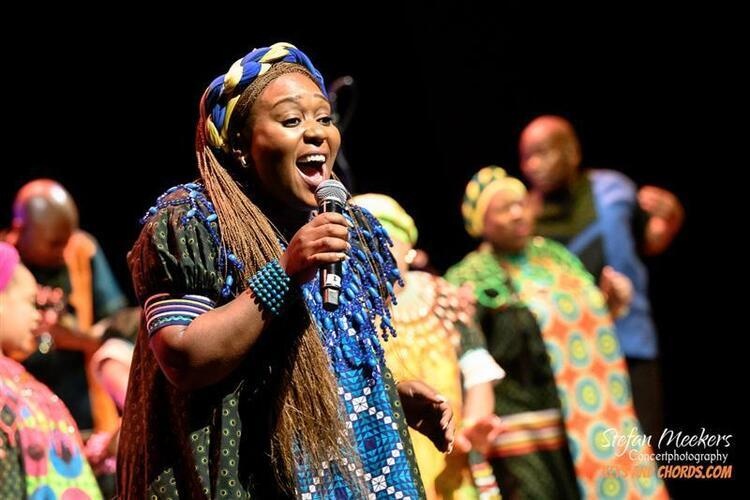 a member of the Soweto Gosepl Choir singing into a microphone with other members in the background
