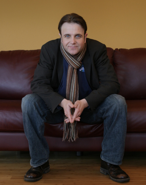 Michael wearing a long brown scarf while sitting on a leather couch