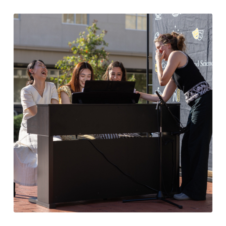 Students singing on Lowry Mall while sitting at a piano.