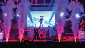 A vibrant rock concert stage with colorful smoke plumes, electric guitars, keyboards, and drums. An energetic atmosphere with a dynamic light show.