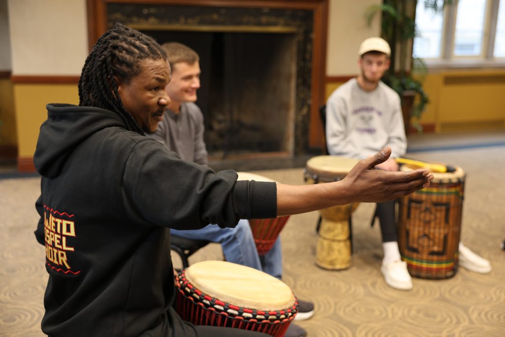 Sipho Ngcamu raises his arm and gestures toward a percussion student across the drum circle.