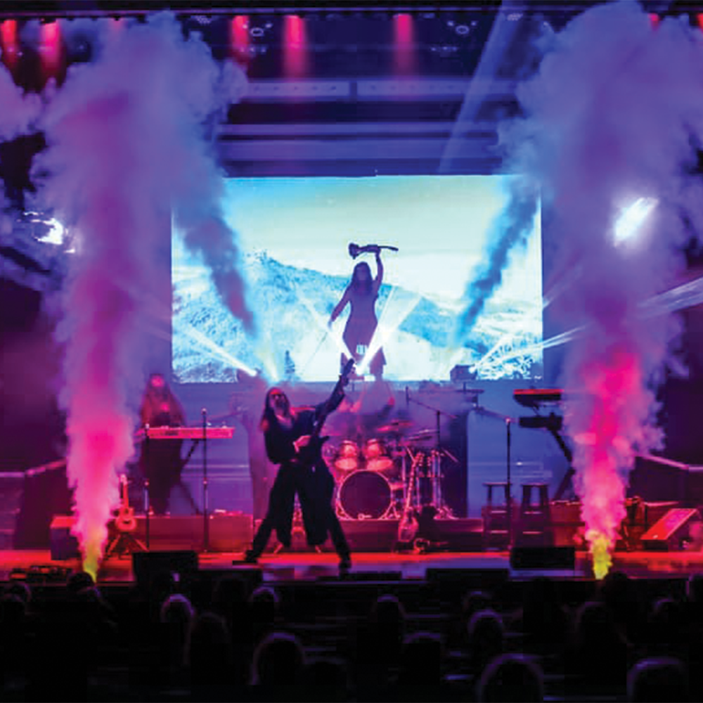 Trans-Siberian players performing on stage with colorful smoke and lights, a giant screen displays a silhouetted figure.