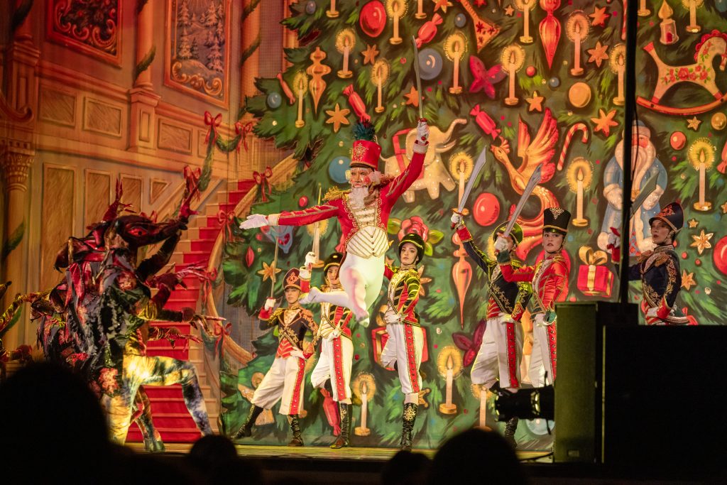 The Nutcracker performer jups on stage amidst a festive holiday backdrop.