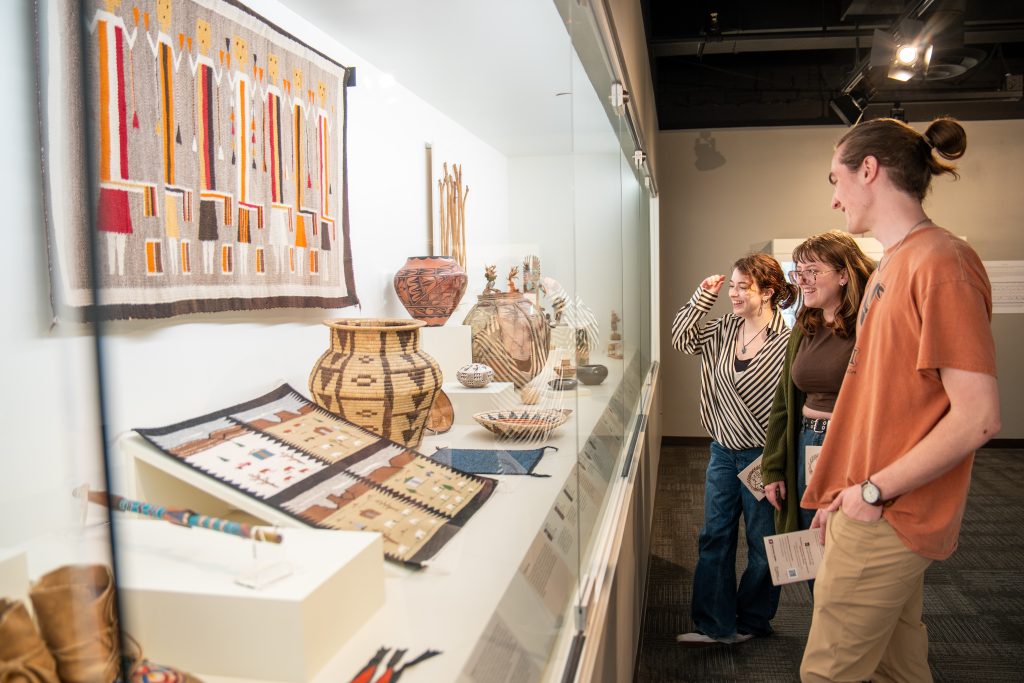 A group of three people stand in front of a display of artefacts at the museum.